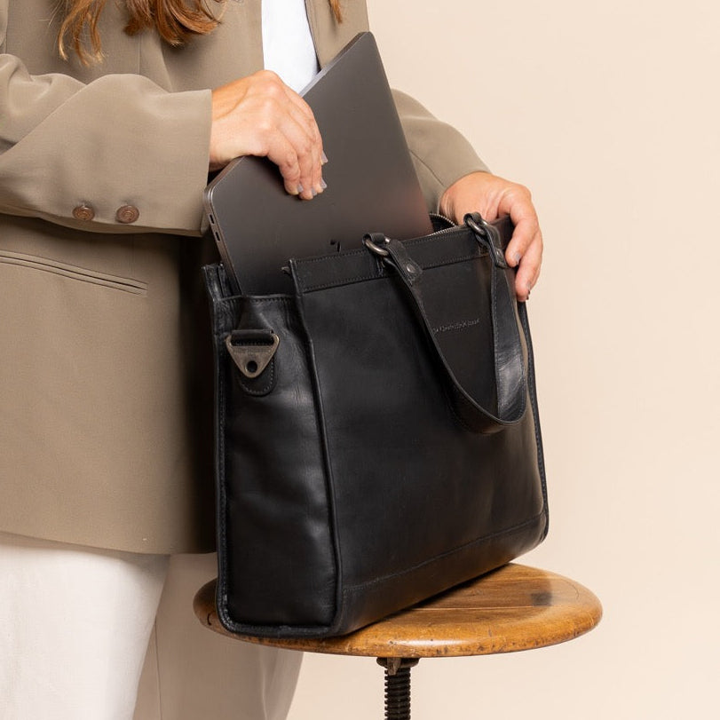 Person holding a black leather briefcase on a wooden stool against a beige background