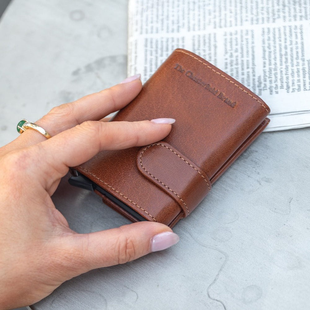 Cognac leather wallet held by a hand on a light gray surface.