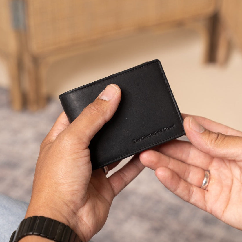 Two hands holding a black leather wallet with a blurred background