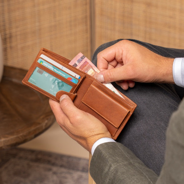 Man sitting on a chair holding a cognac leather wallet with cards and money.