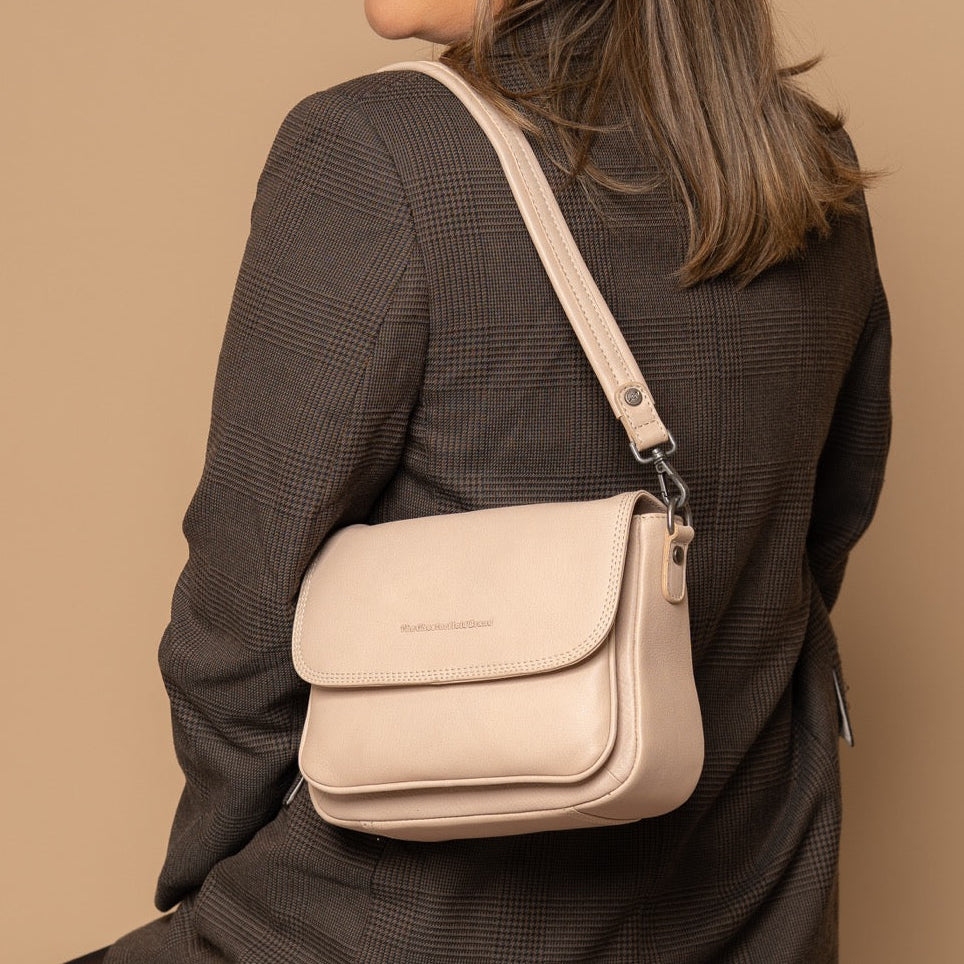Woman sitting on a stool wearing a beige crossbody bag against a beige background