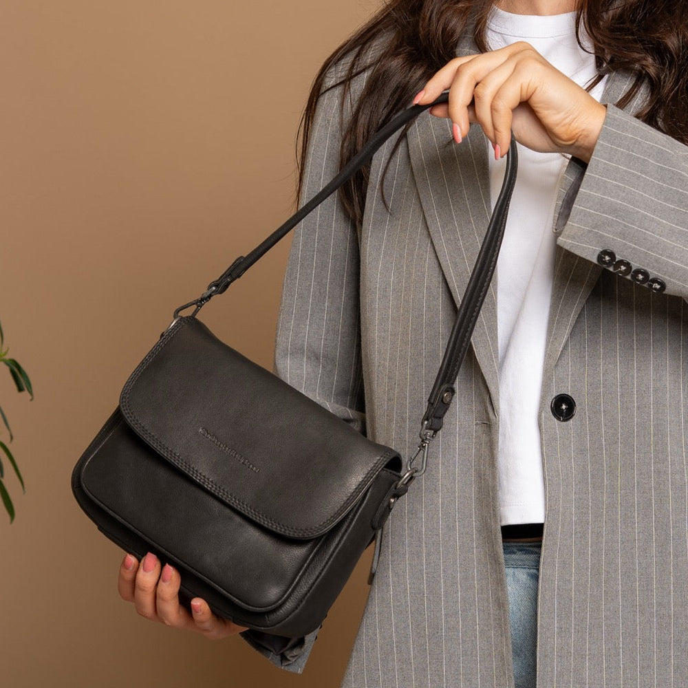 Woman holding a black handbag against a beige background
