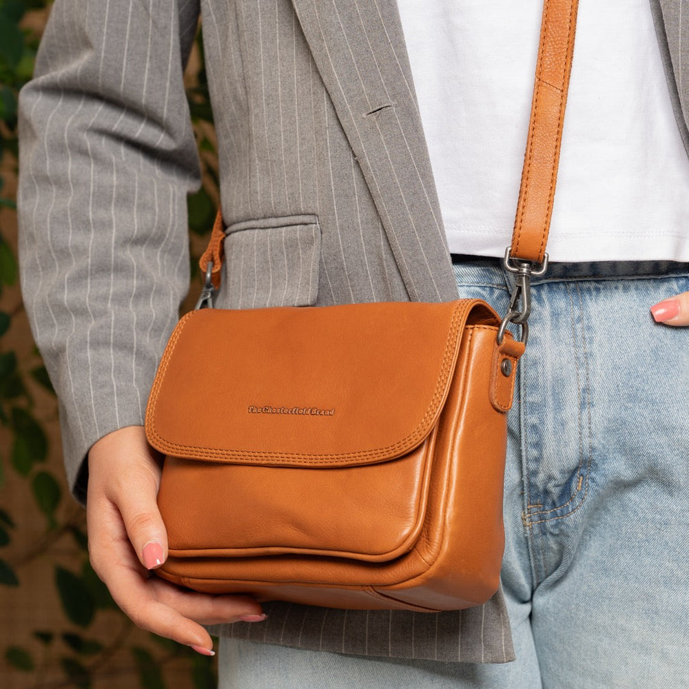 Person holding a cognac leather bag with a blurred background