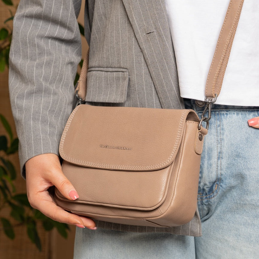 Person wearing a beige crossbody bag with a neutral background