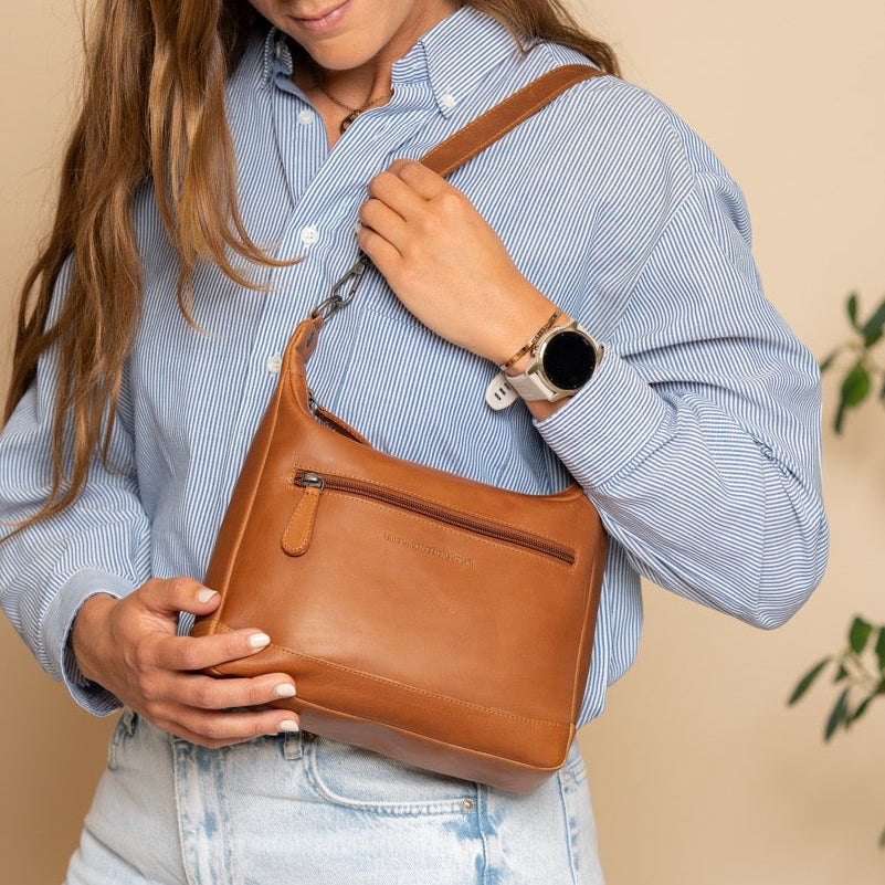 Woman holding a cognac leather handbag against a beige background