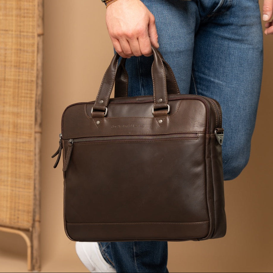 Person holding a brown leather briefcase in an indoor setting