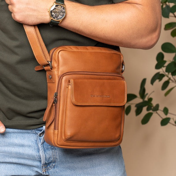 Man wearing a green t-shirt and blue jeans with a cognac leather crossbody bag.