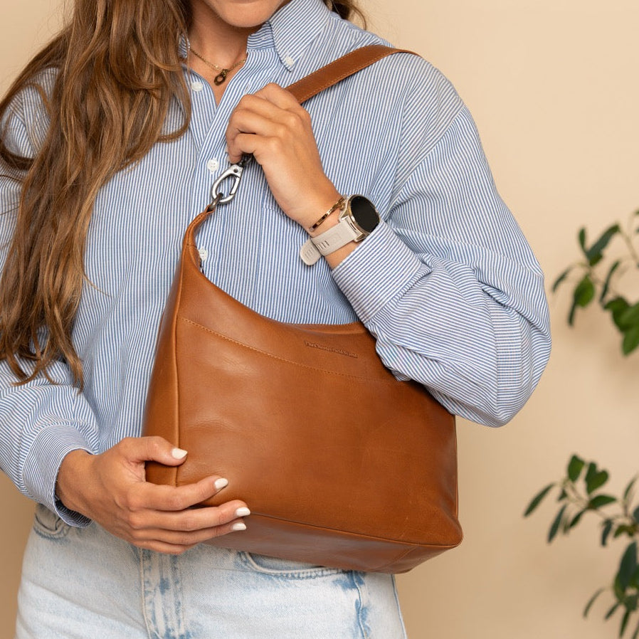 Woman holding a cognac leather bag against a beige wall