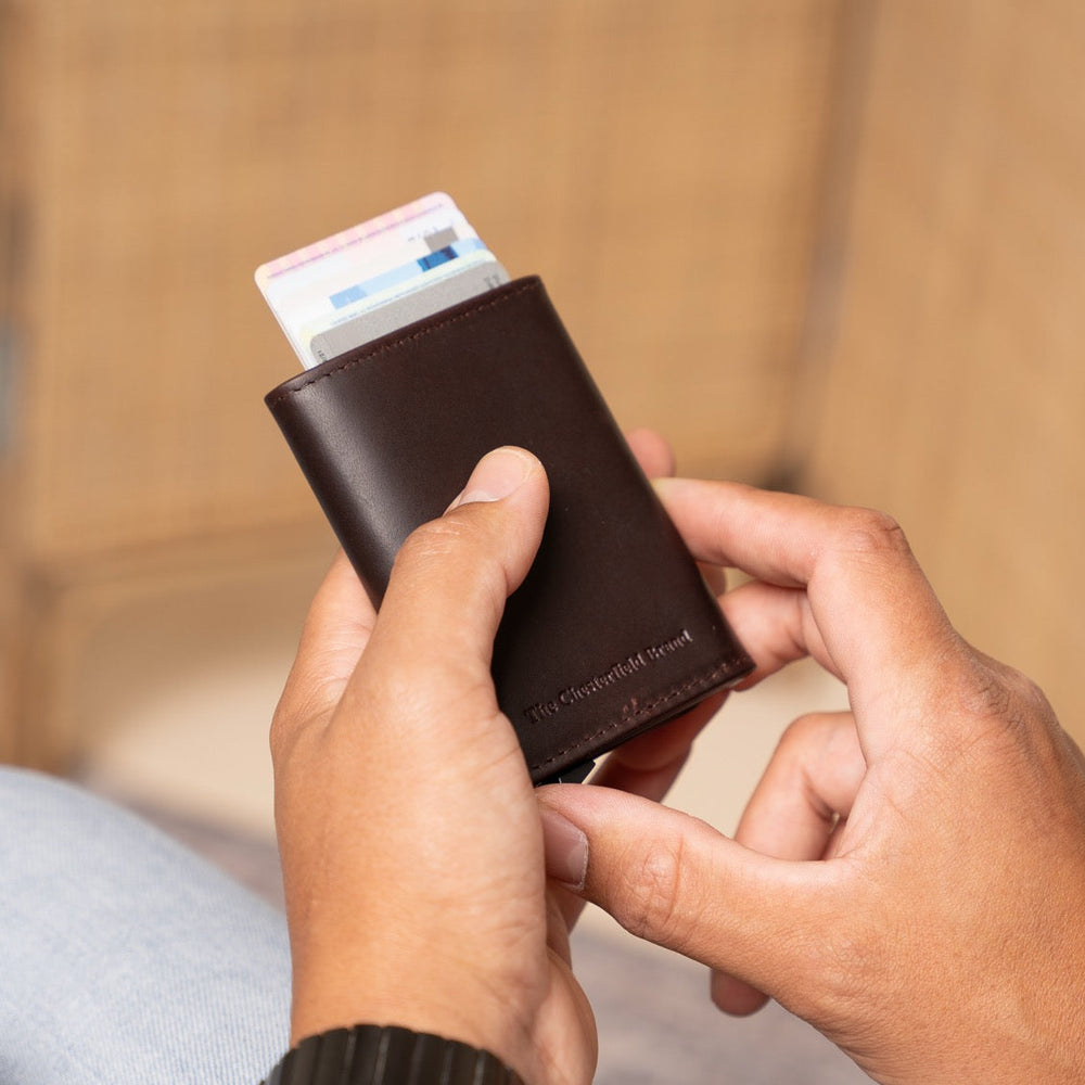 Person holding a brown wallet with cards against a blurred background