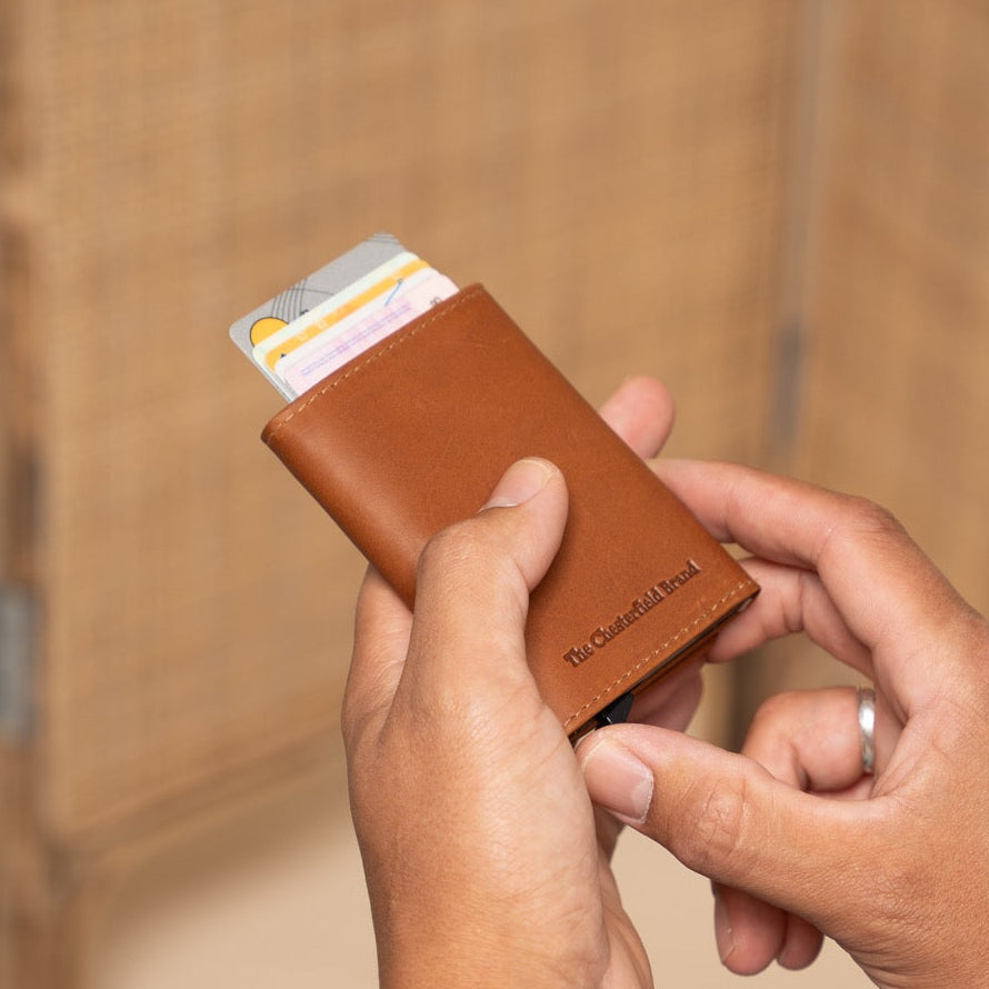 Person holding a cognac leather wallet with cards against a wooden background