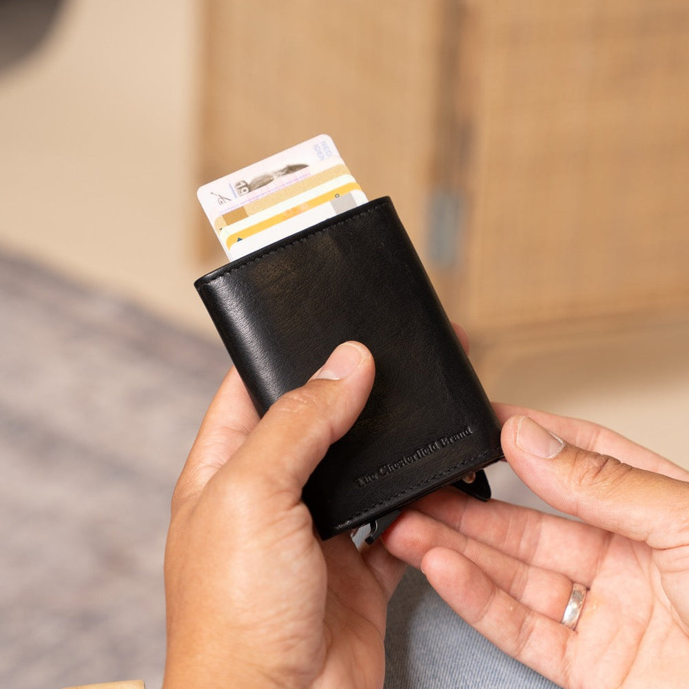Person holding a black wallet with cards, sitting on a wooden chair.