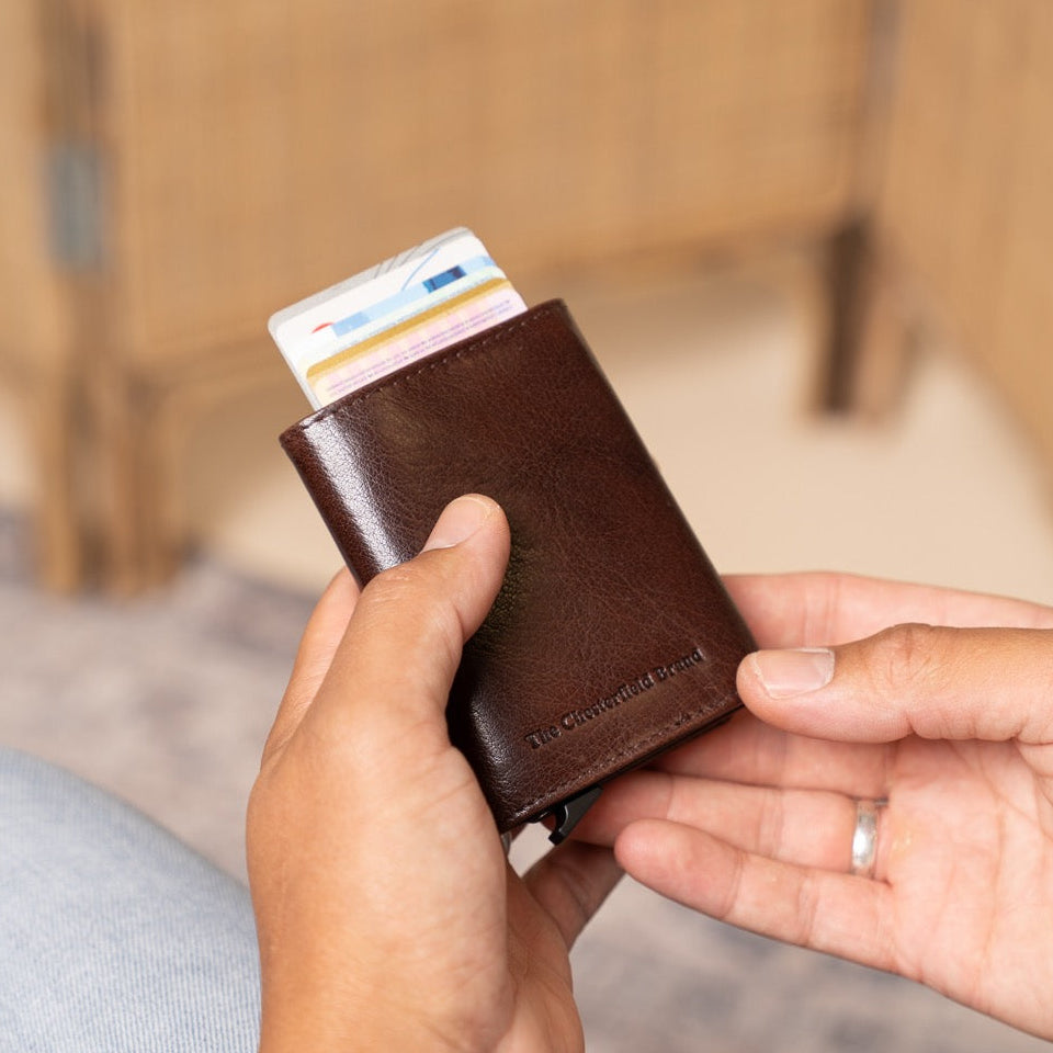 Person holding a brown leather wallet with cards, sitting on a couch.
