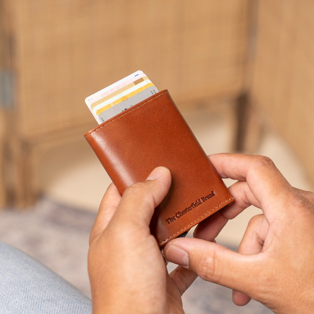 Person holding a cognac leather wallet with cards, blurred background