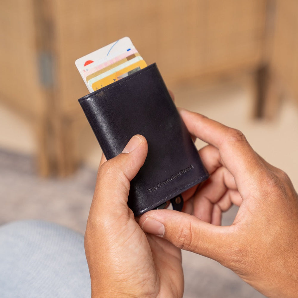 Person holding a navy leather wallet with cards, sitting on a wooden floor.