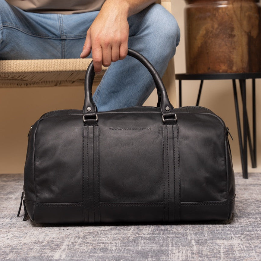Person sitting on a chair with a black duffel bag in front of them, indoor setting.