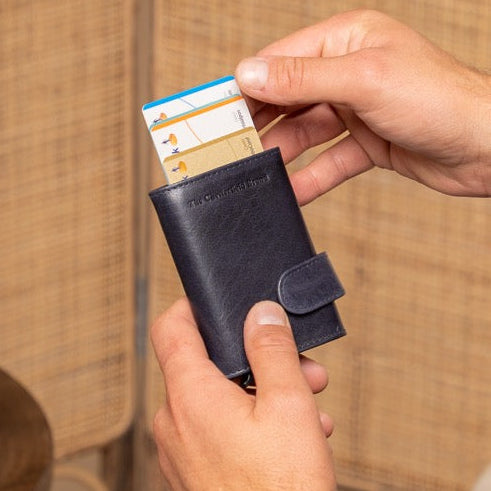 Man in a suit holding a card in a navy card holder against a woven wall.