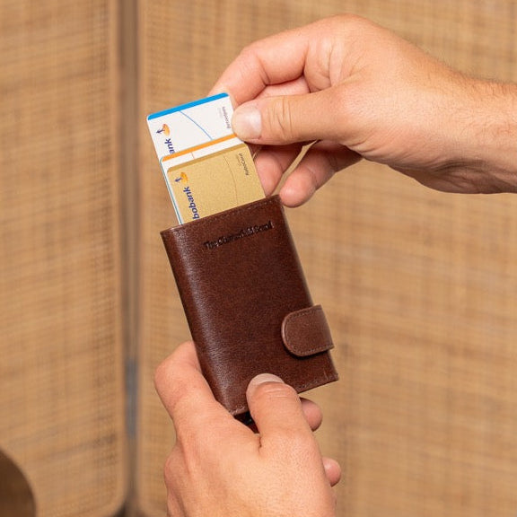 Man in a suit holding a brown leather wallet with cards against a neutral background