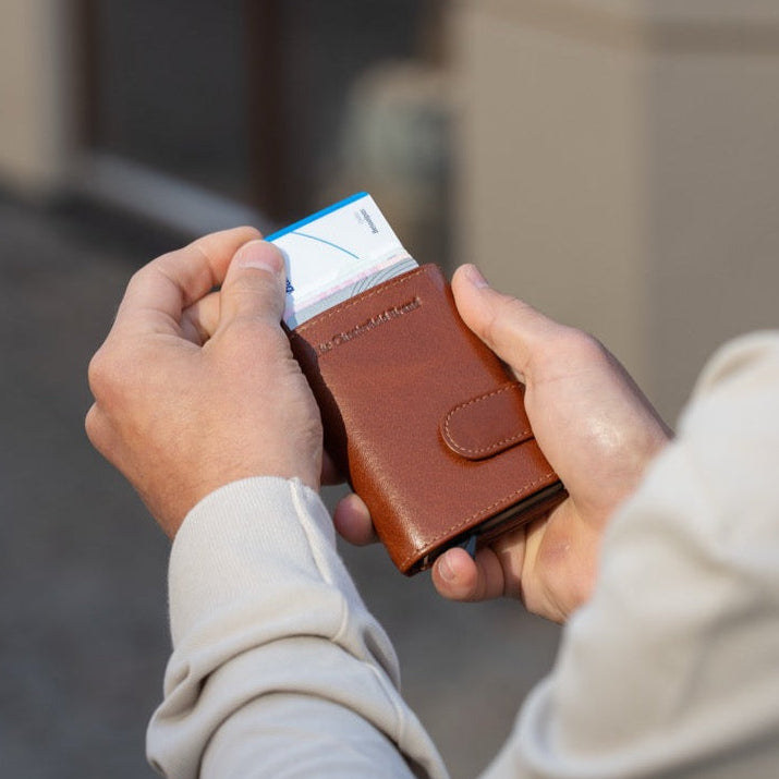Person holding a cognac leather wallet with a blurred background