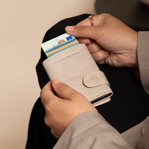 Person holding a wallet with cards in a room with a vase on a table.