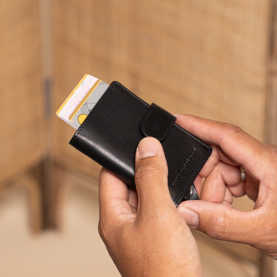 Person holding a black wallet with a card, sitting on a wooden floor.