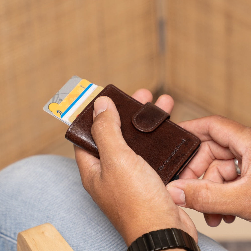 Person holding a brown leather wallet with a card inside, sitting on a wooden chair.