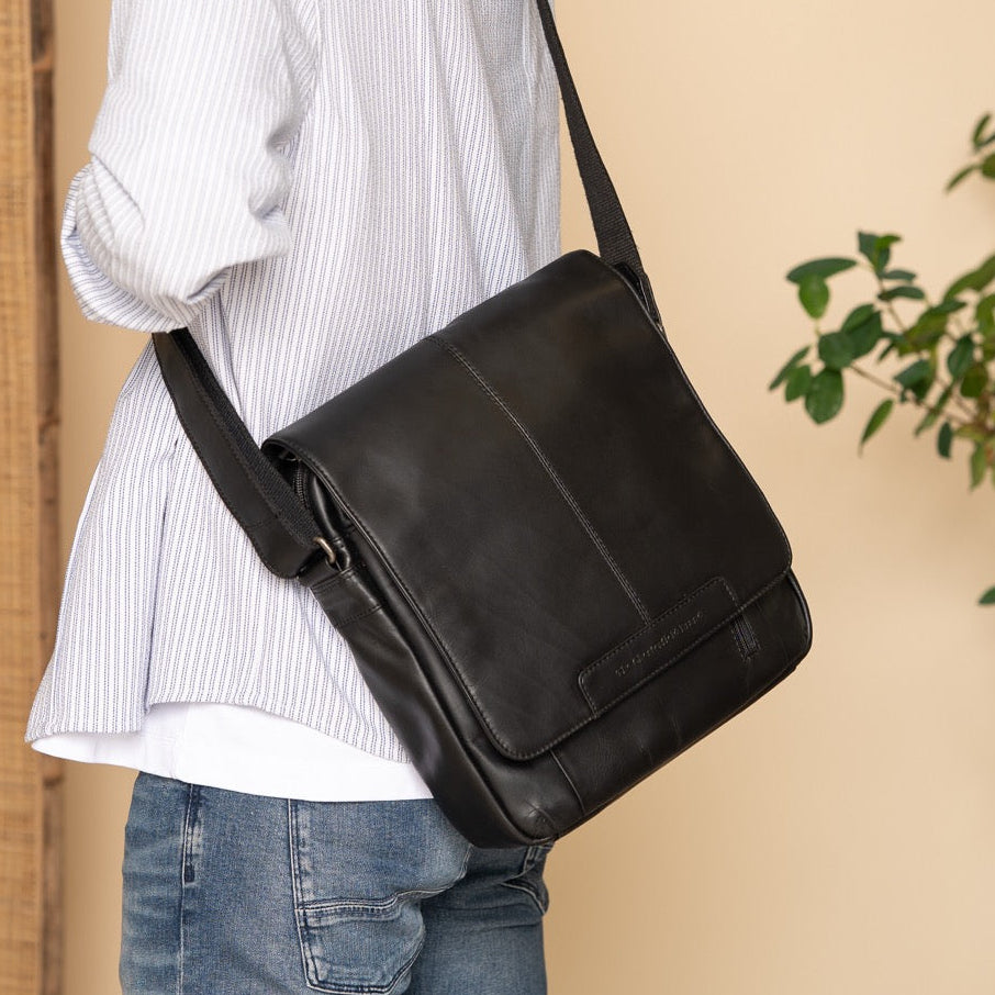 Person wearing a black shoulder bag against a beige wall with a plant in the corner