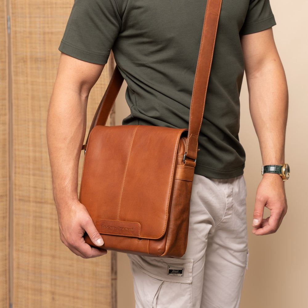 Person holding a cognac leather bag against a beige background