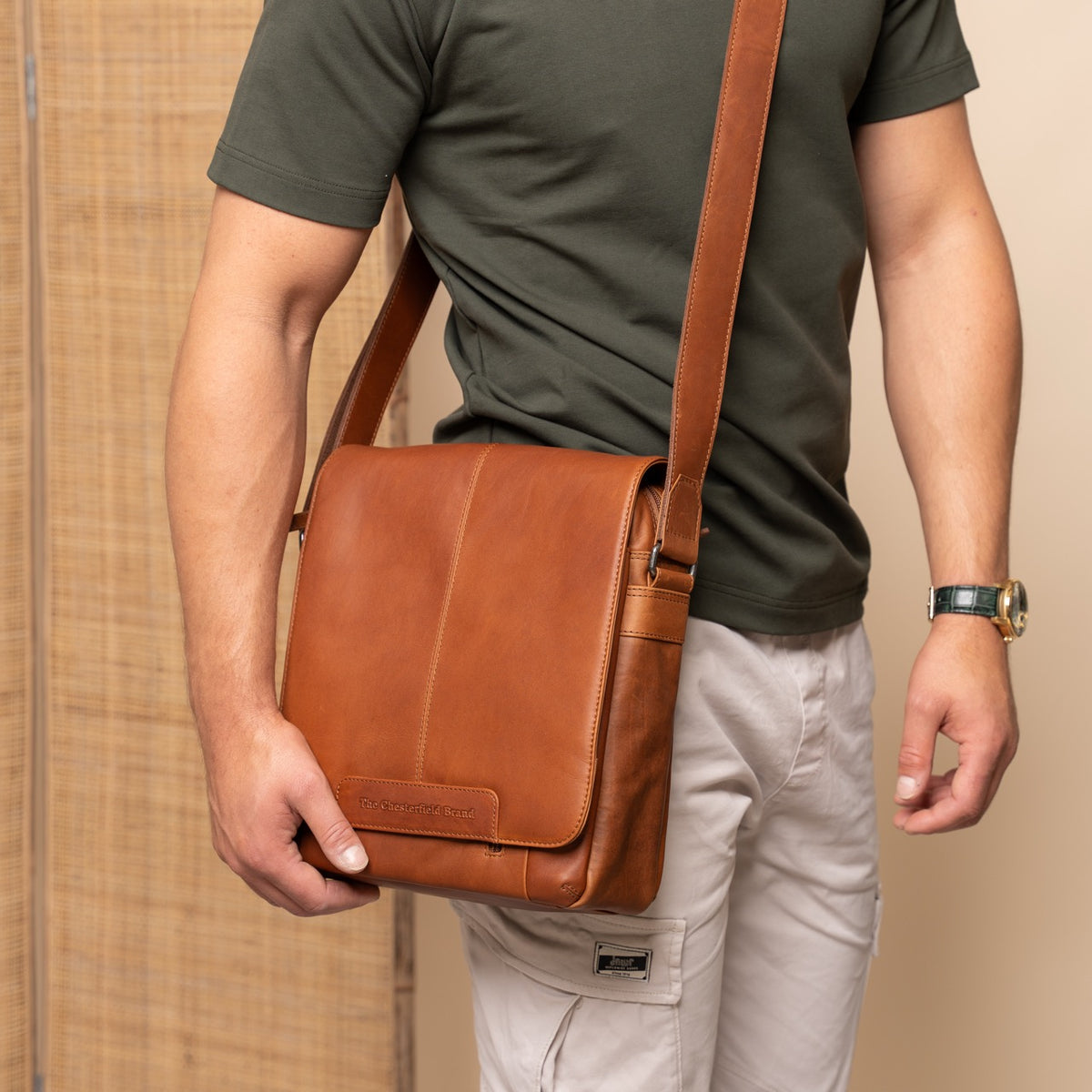 Person holding a cognac leather bag against a beige background