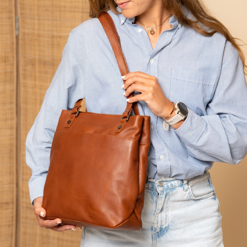 Woman holding a cognac leather bag against a beige background