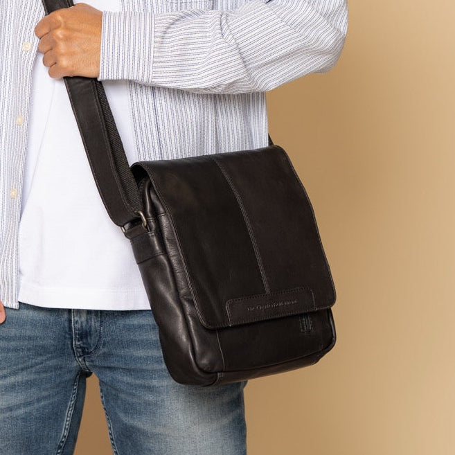 Man holding a black leather bag against a beige background