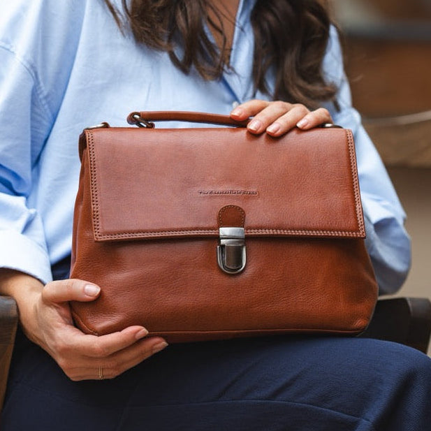 Woman holding a cognac leather handbag in an indoor setting