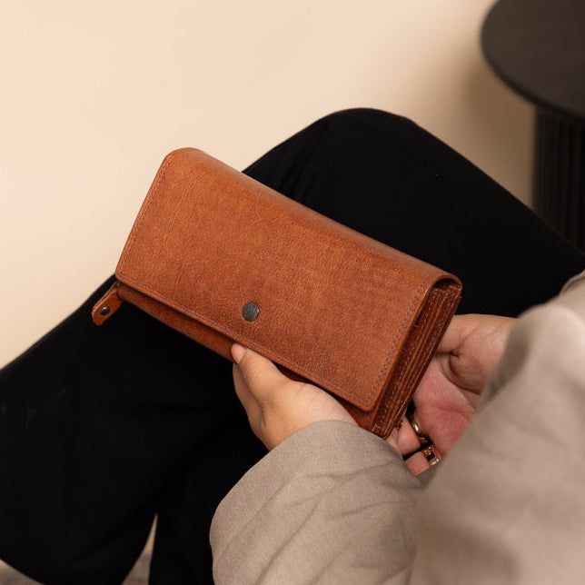 Women sitting on a chair holding a cognac leather wallet.