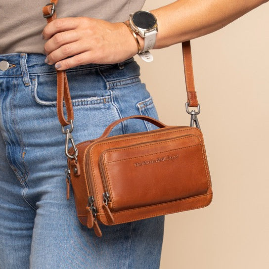 Woman holding a cognac leather shoulder bag against a beige background
