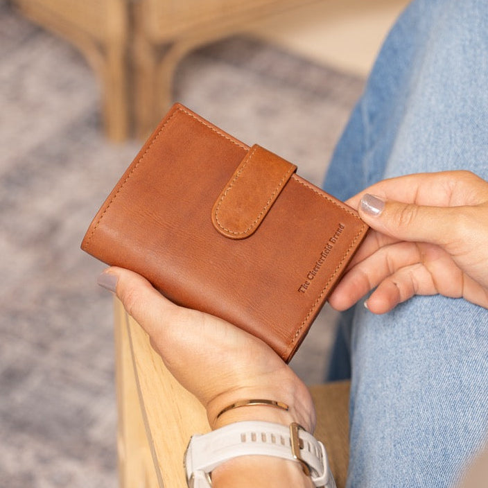 Person holding a cognac leather wallet with a blurred background