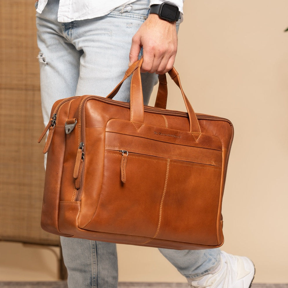 Men holding a cognac leather laptop bag with a beige blurred background