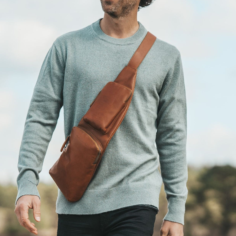 Man walking outdoors with a cognac crossbody bag, smiling
