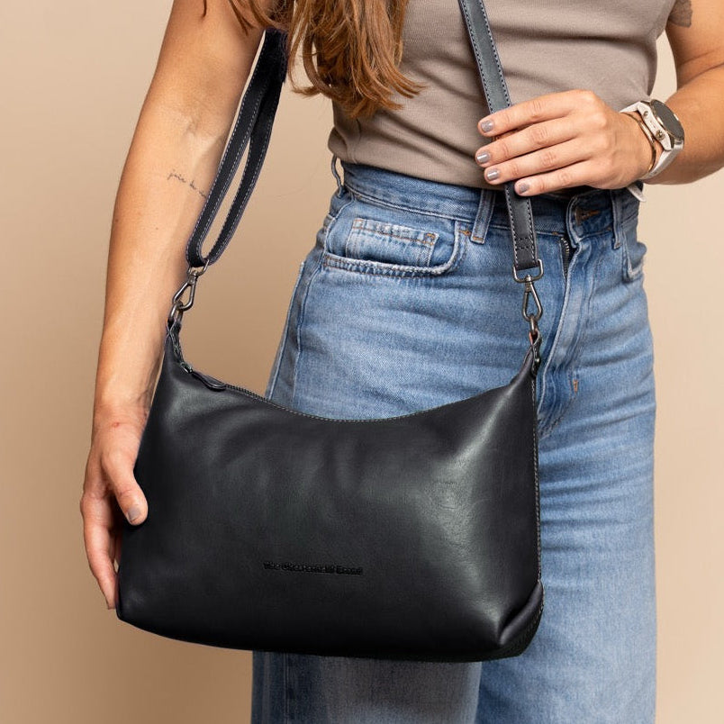 Person holding a black leather handbag against a beige background