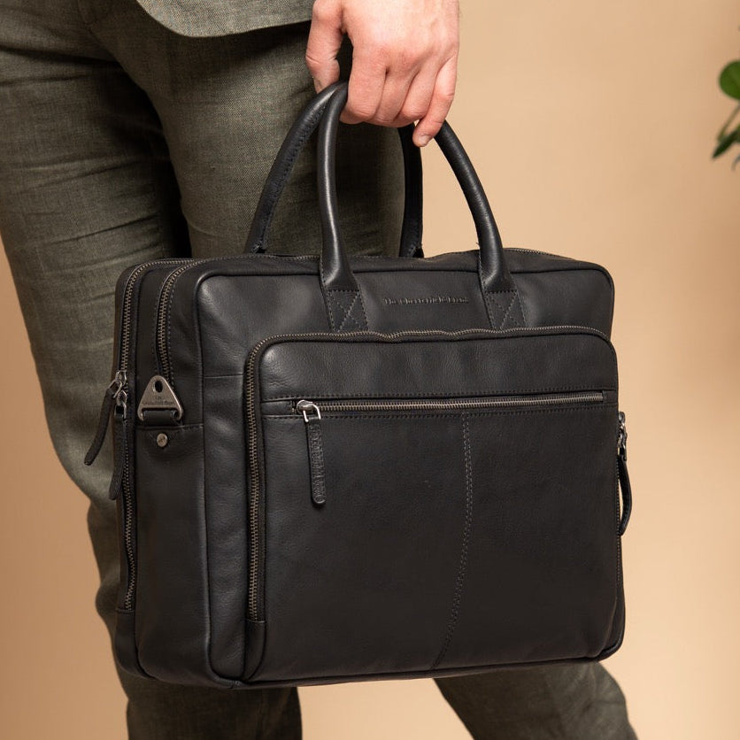 Person holding a black laptop bag against a beige wall with a plant in the corner