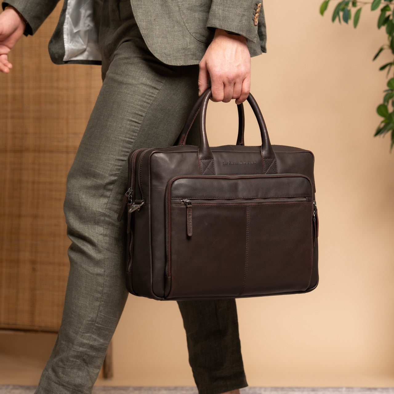 Person holding a brown leather briefcase against a beige background