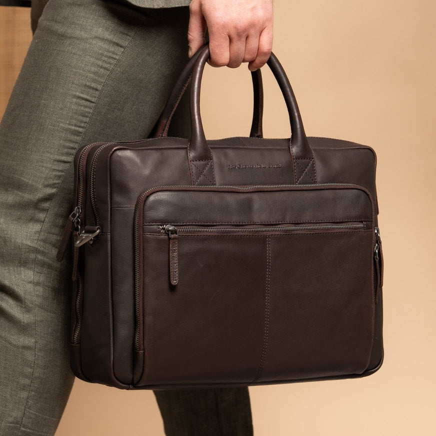 Person holding a brown leather briefcase against a beige background