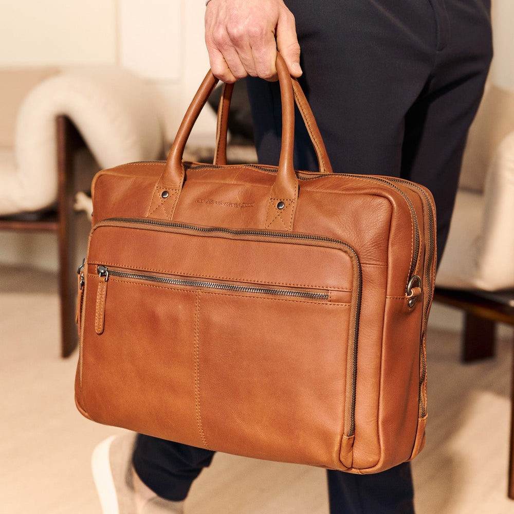 Person holding a cognac leather briefcase in an indoor setting