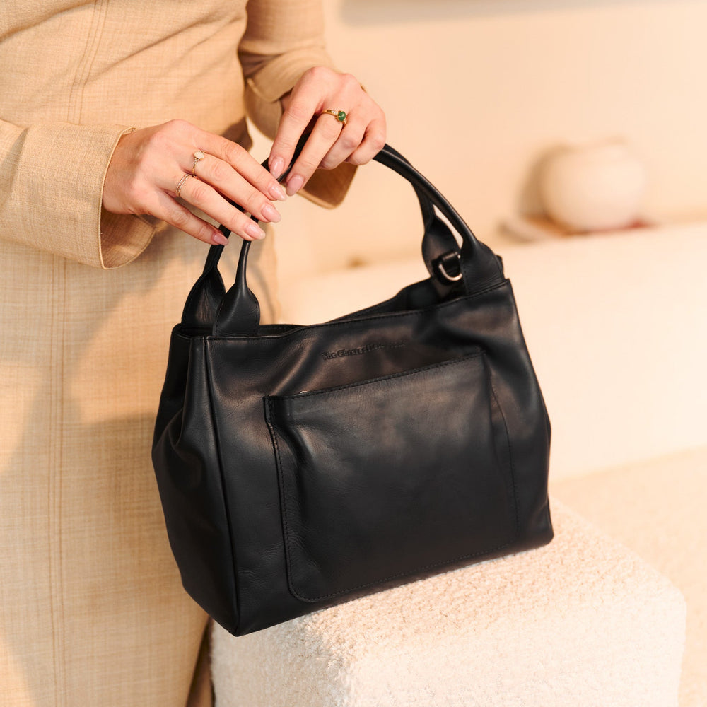 Person holding a black leather handbag with a blurred background