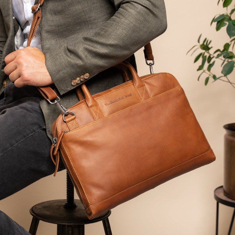 Man holding a cognac leather briefcase in an indoor setting