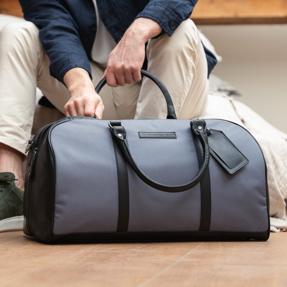 Person holding a gray duffel bag on a wooden floor.