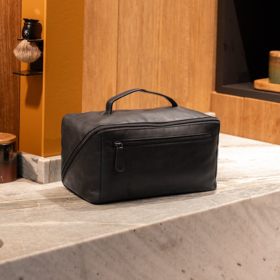 Black leather toiletry bag in a premium bathroom setting with marble and wood details