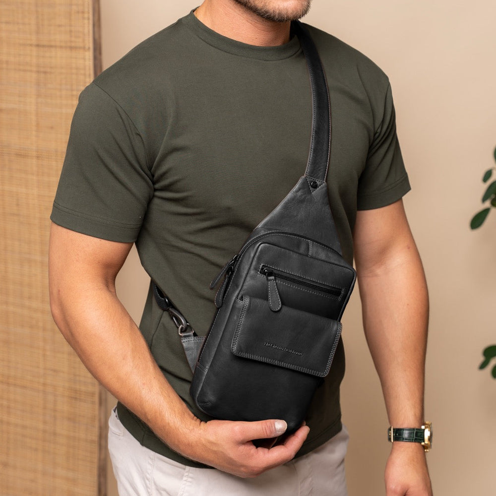 Man holding a black sling bag against a beige background