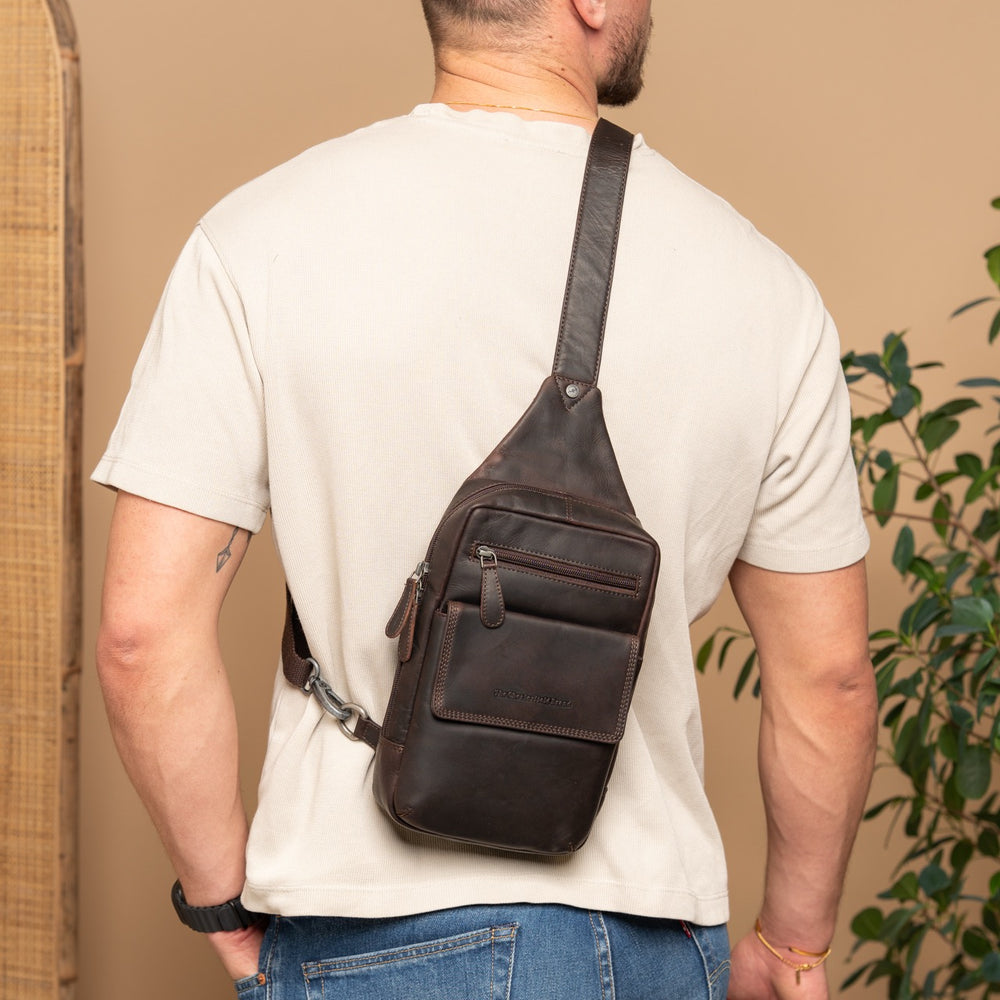 Man wearing a black sling bag over one shoulder against a beige wall.