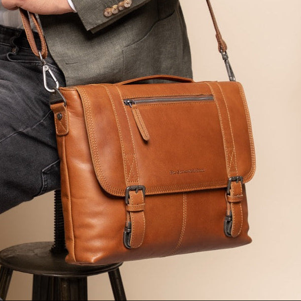 Man holding a cognac leather bag against a beige wall