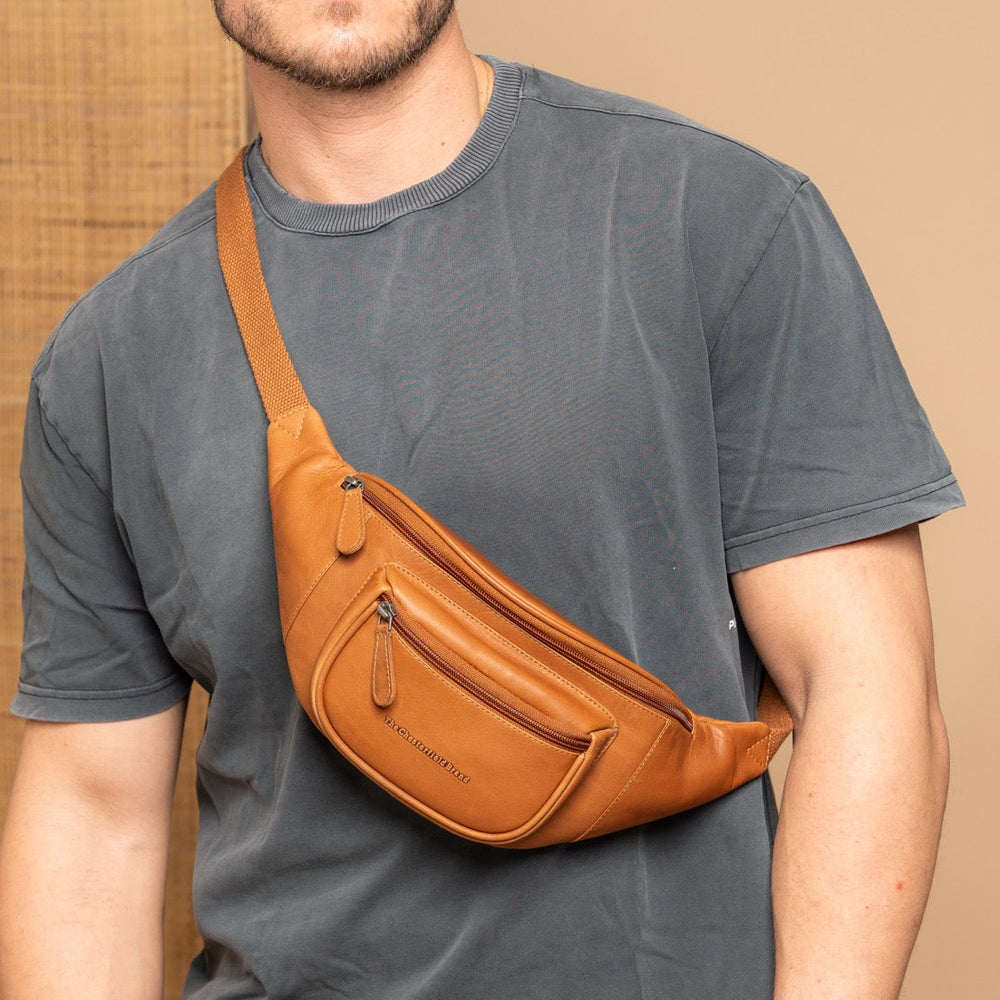 Man wearing a cognac leather fanny pack over his shoulder against a beige background