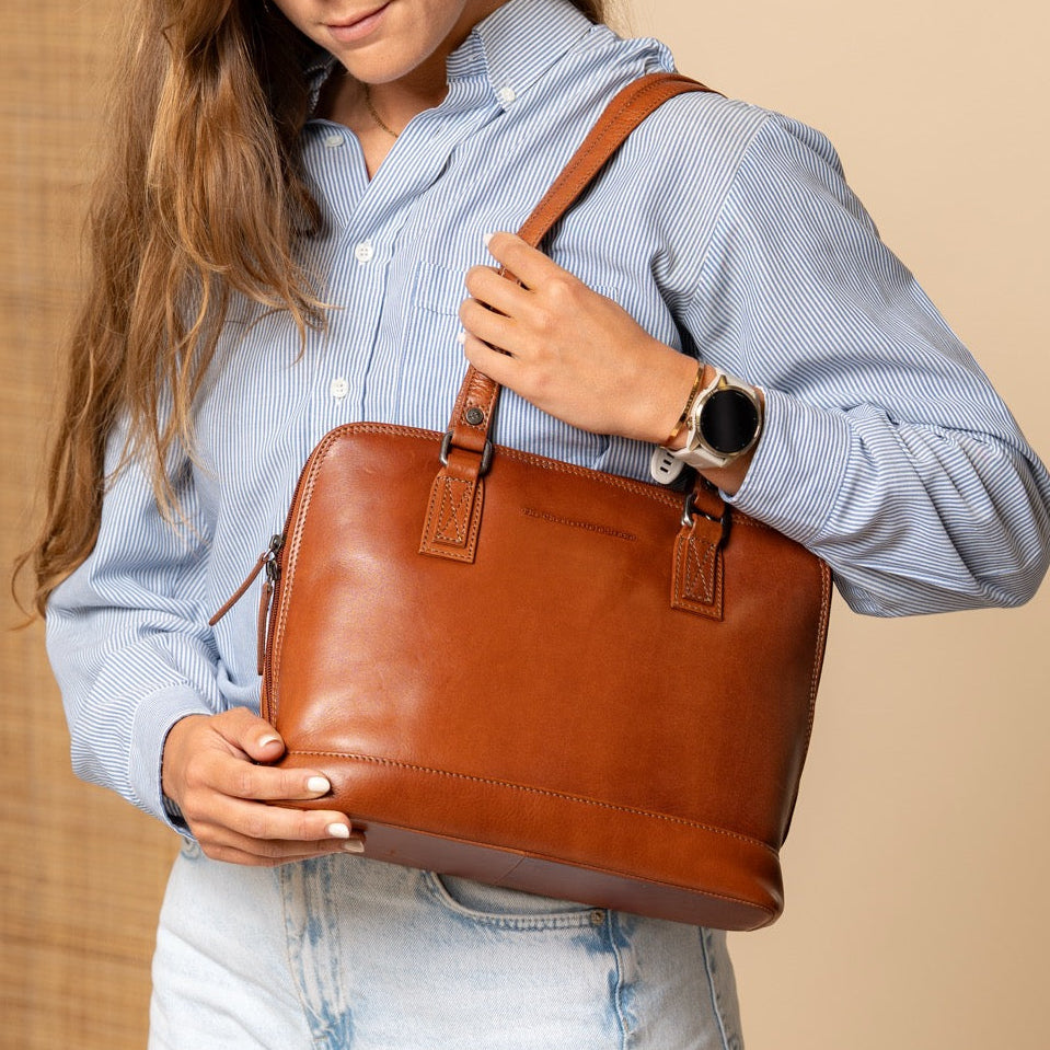 Woman holding a cognac leather bag against a beige background